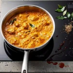 Sizzling tempering being mixed into a simmering pan of Punjabi curry next to a smartphone displaying recipe analytics.