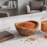 Raw red lentils and a jar of finely ground masoor dal powder arranged on a stylish desk representing organic skincare ingredients.